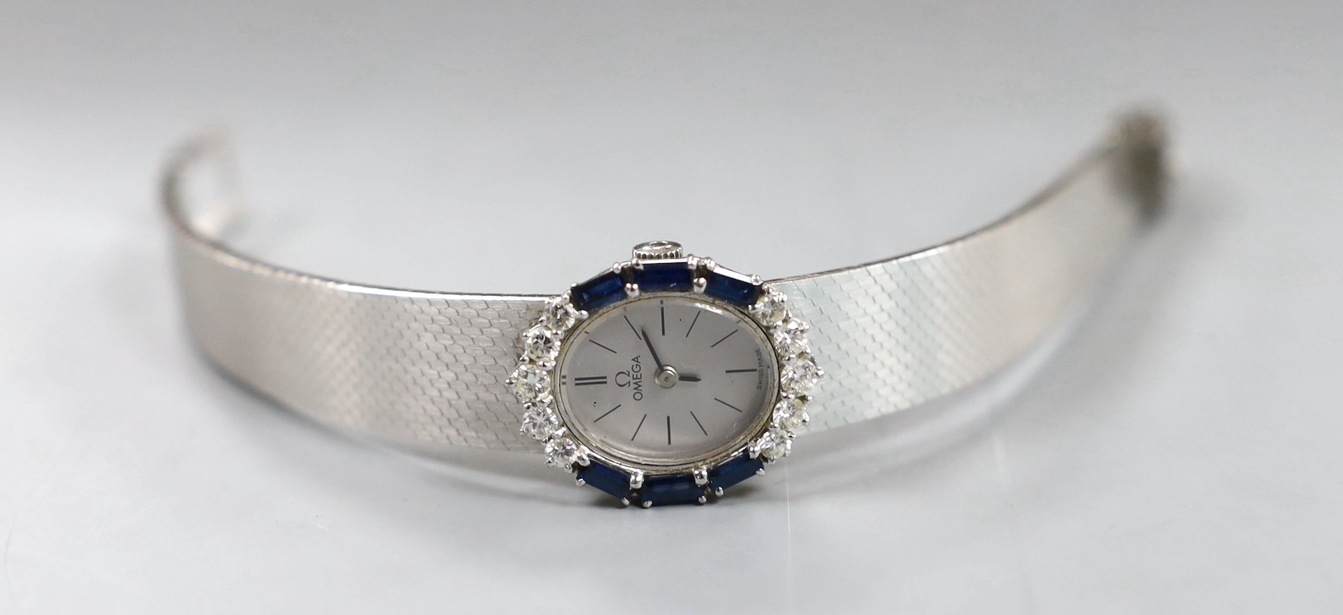 A lady's French 750 white metal Omega manual wind oval wrist watch, with sapphire and diamond set bezel, on integral Omega 750 white metal bracelet, overall 17.7cm, gross weight 52.5 grams, no box or papers.